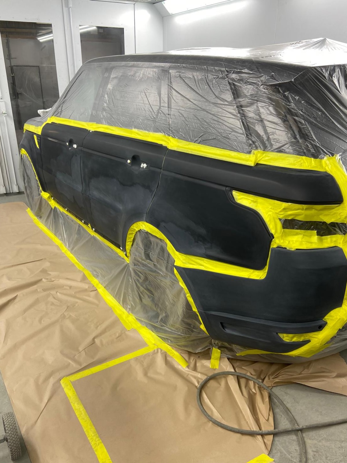 Range Rover Sport in Santorini black masked up in the spray booth, with the doors and rear bumper prepped for a full respray after poor previous paintwork
