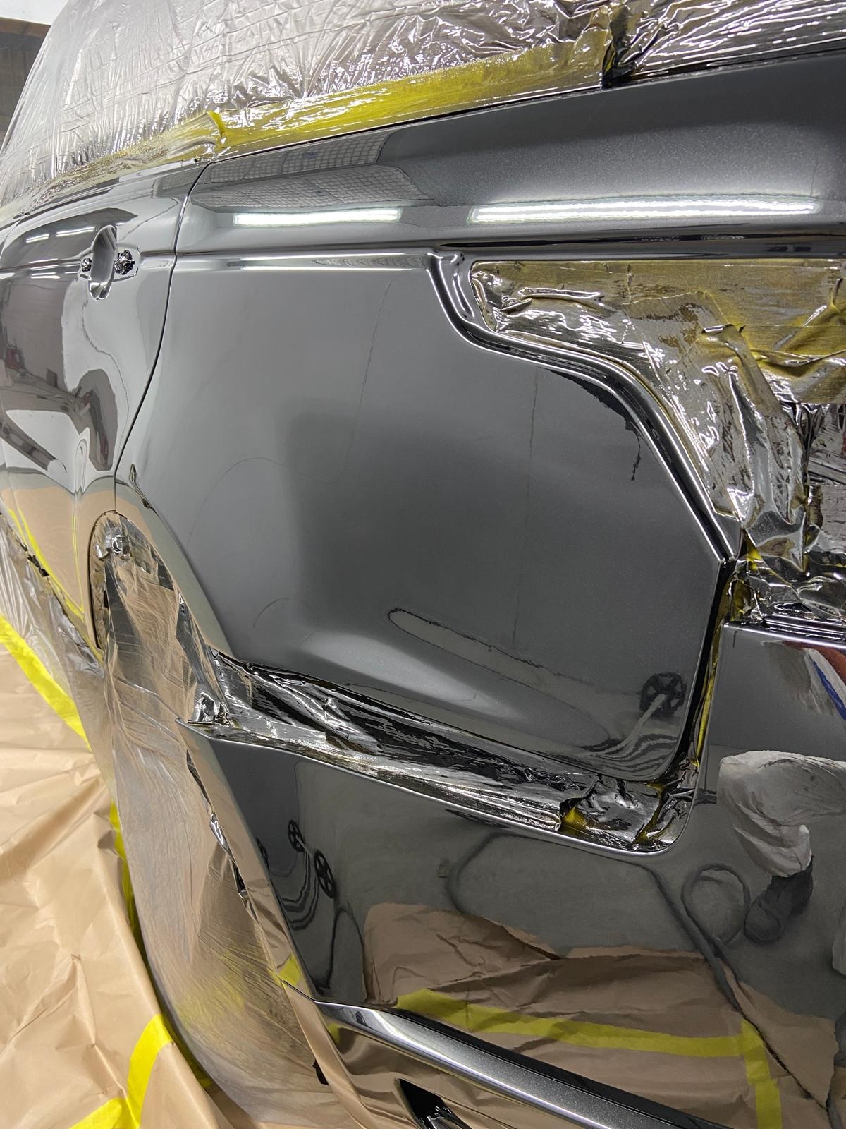 Close-up of the freshly painted rear quarter panel in gloss black, still masked at the edges while the paint cures