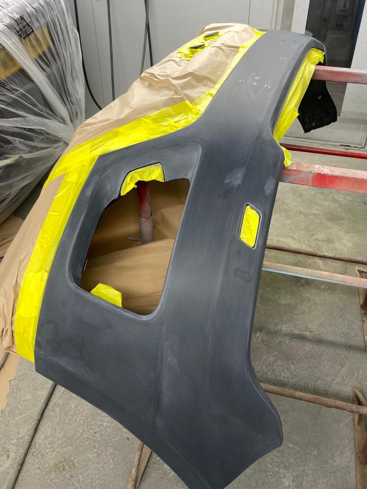 Rear bumper cover removed from the car and mounted on a paint stand, masked up in grey primer ready for colour