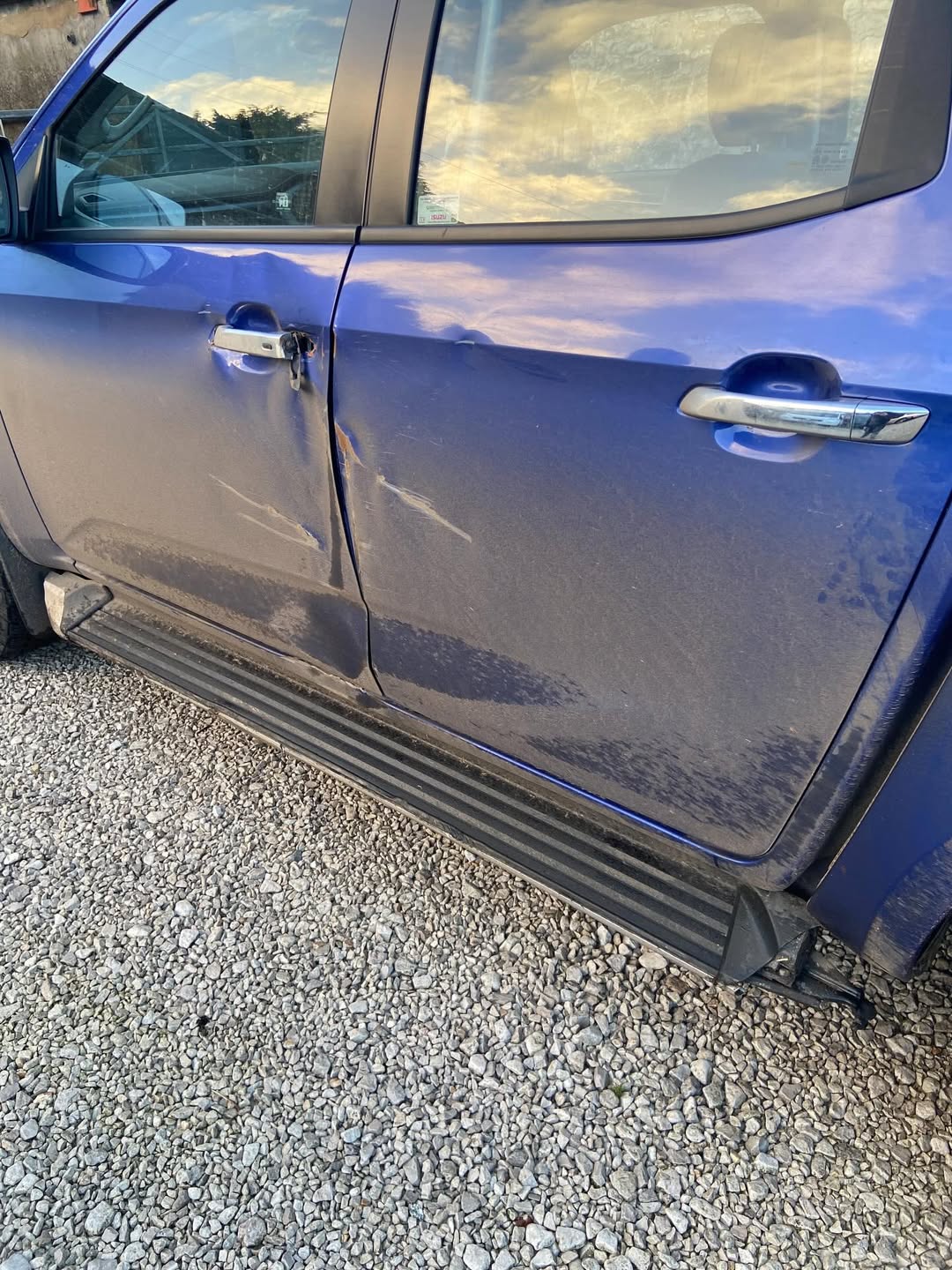 Deep scuffs and paint damage along the front door and sill of a dark blue Isuzu D-Max