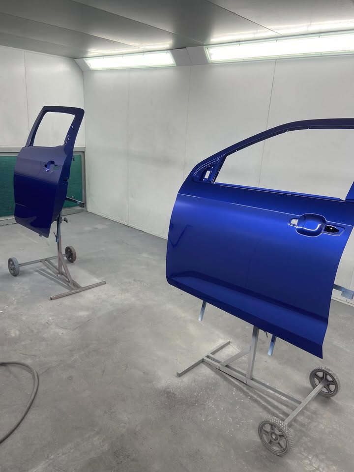 Two new replacement doors mounted on paint stands in the spray booth, freshly painted dark blue