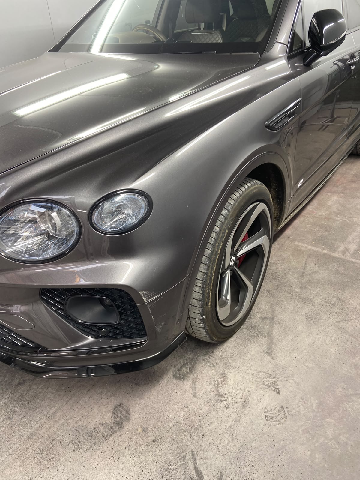 Bentley Bentayga nearside front wing and bumper corner before repair, with a deep scuff and paint transfer down towards the wheel arch