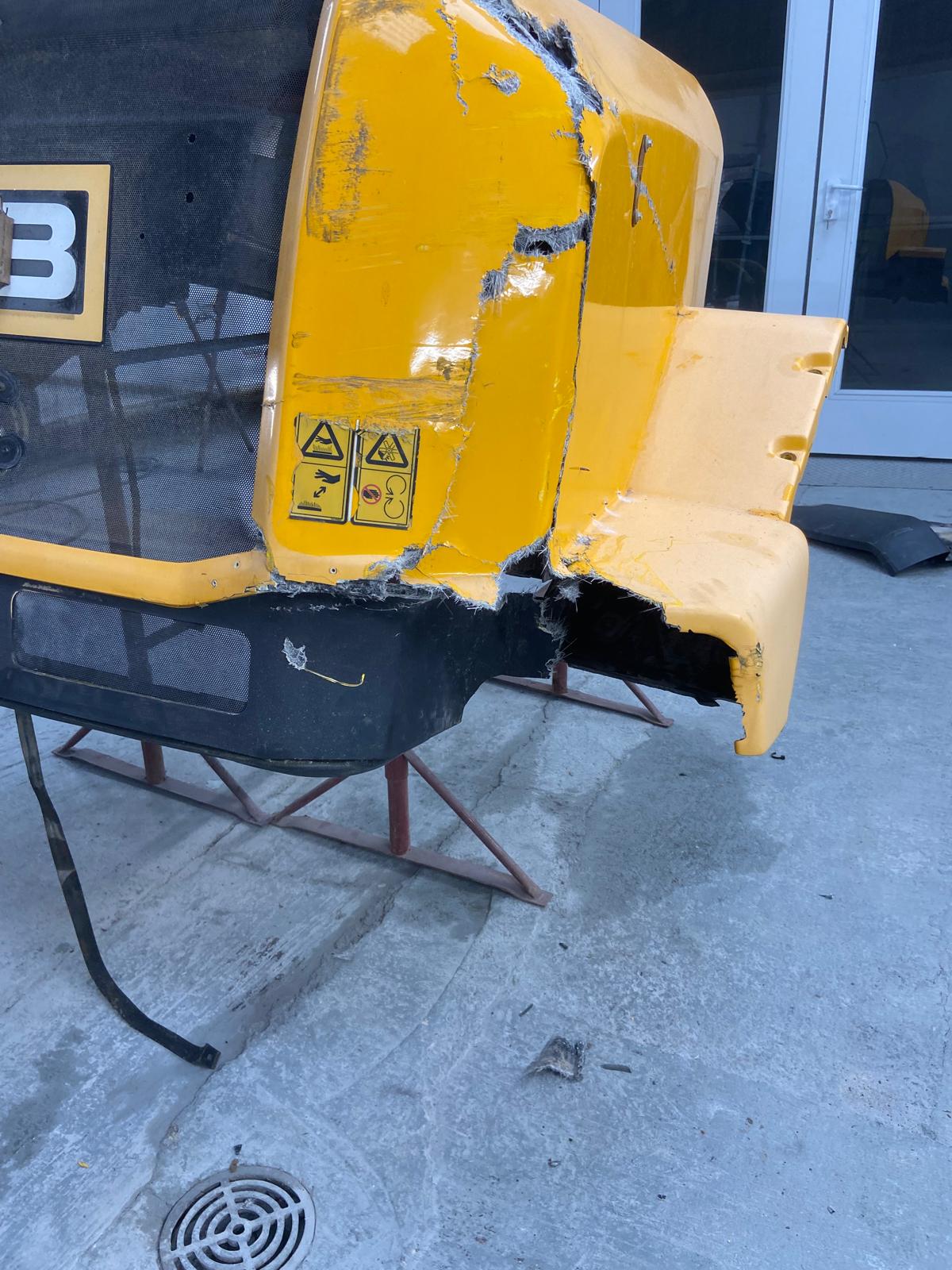 Smashed JCB loading shovel bonnet panel, with the fibreglass cracked and torn open at the rear corner