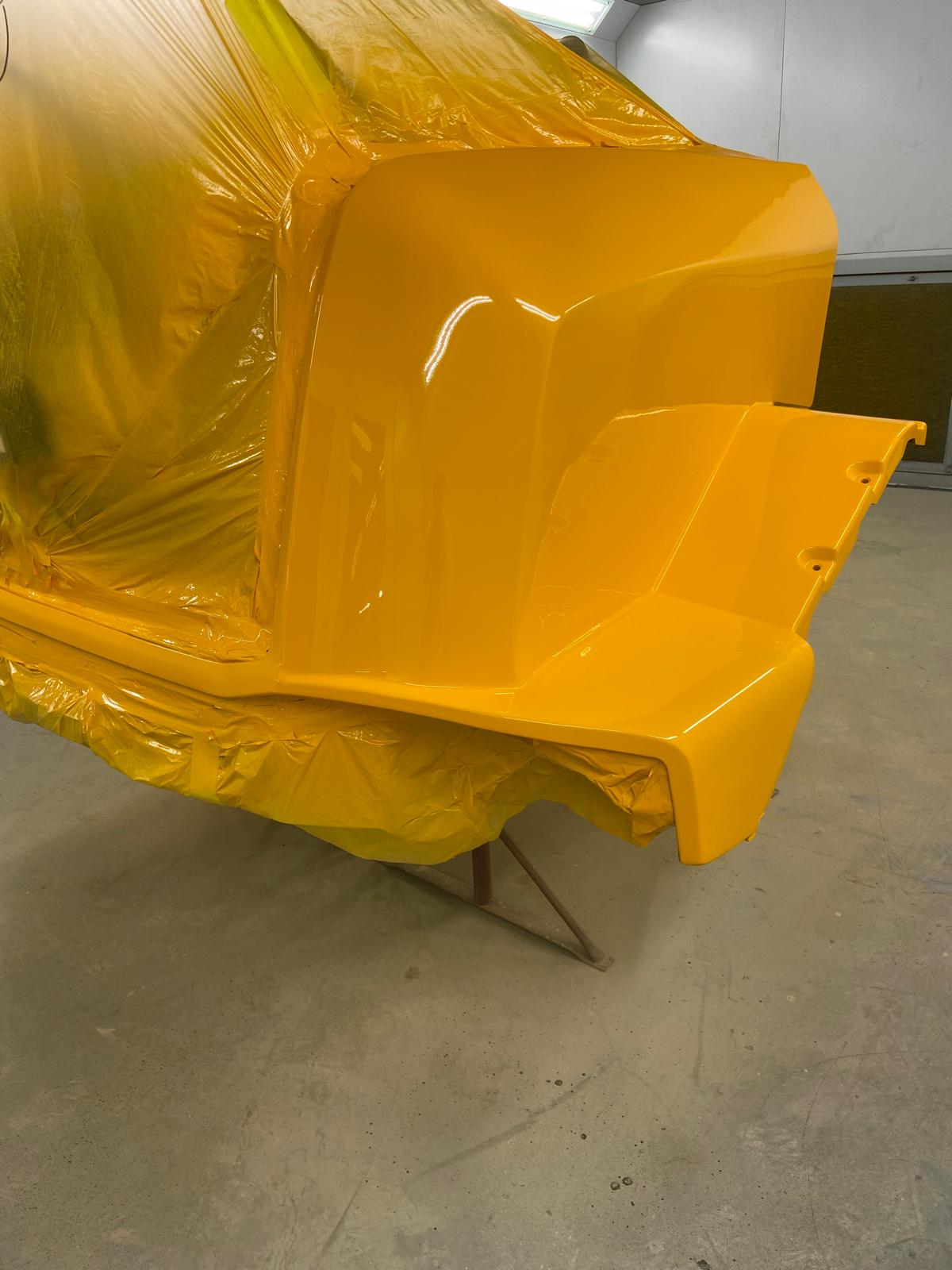 Repaired JCB loading shovel bonnet panel freshly painted in gloss JCB yellow, still wrapped up while the paint cures