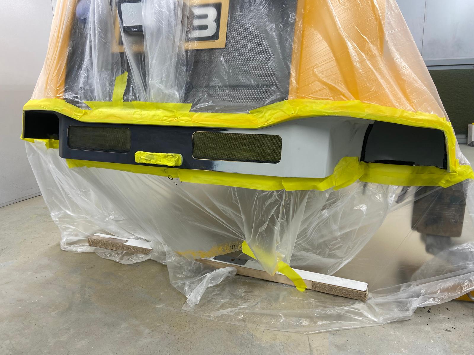 JCB loading shovel front grille panel masked up in the spray booth, with the mesh guards protected ready for colour